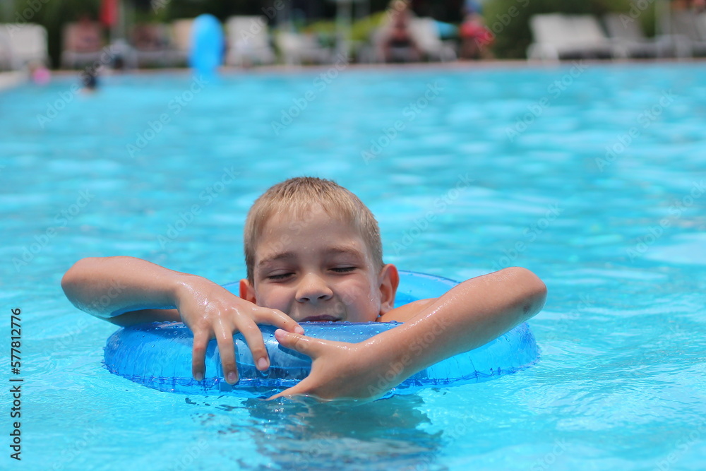 Funny little boy swims in a pool in an blue life preserver