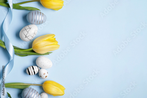 Flat lay composition with tulips and beautifully painted eggs on light blue background, space for text. Easter celebration