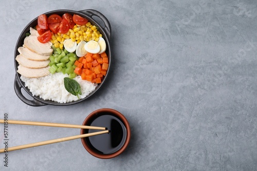 Delicious poke bowl with different ingredients, chopsticks and soy sauce on grey table, flat lay. Space for text