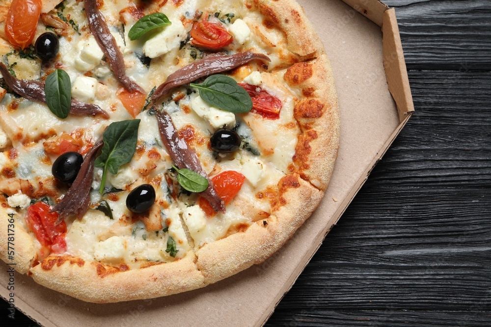 Tasty pizza with anchovies, basil and olives on black wooden table, top view