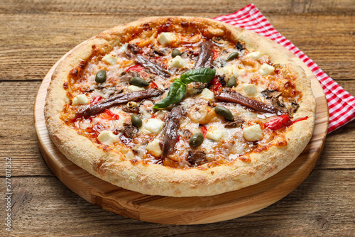 Tasty pizza with anchovies, basil and olives on wooden table