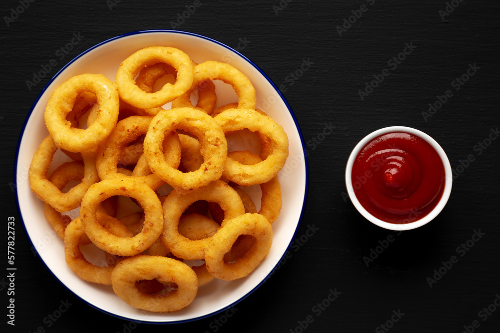 Homemade Breaded Onion Rings with Ketchup on a Plate on a black background, top view. Flat lay, overhead, from above. Homemade Breaded Onion Rings with Ketchup on a Plate on a black background, top view. Flat lay, overhead, from above.