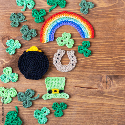 St Patrick's Day concept. Knitted composition of a green hat, a pot of gold, a horseshoe, a rainbow and green shamrocks on a wooden background