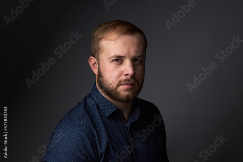Portrait of a young confident blonde in a dark shirt, with a beard on a dark background © justoomm