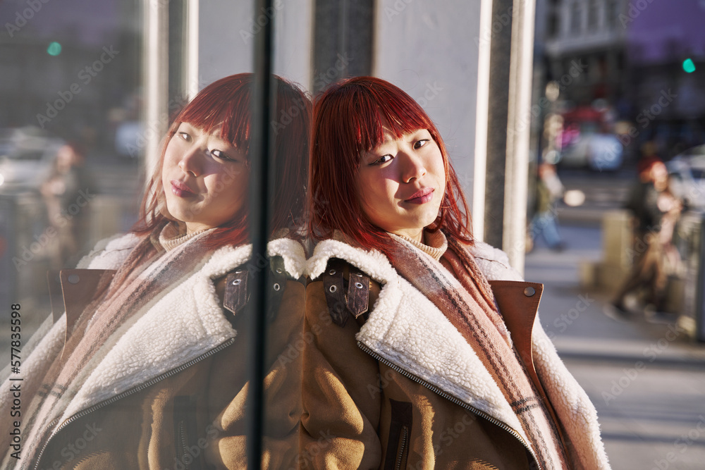 Portrait of a young Chinese woman leaning against a glass showing her reflection.