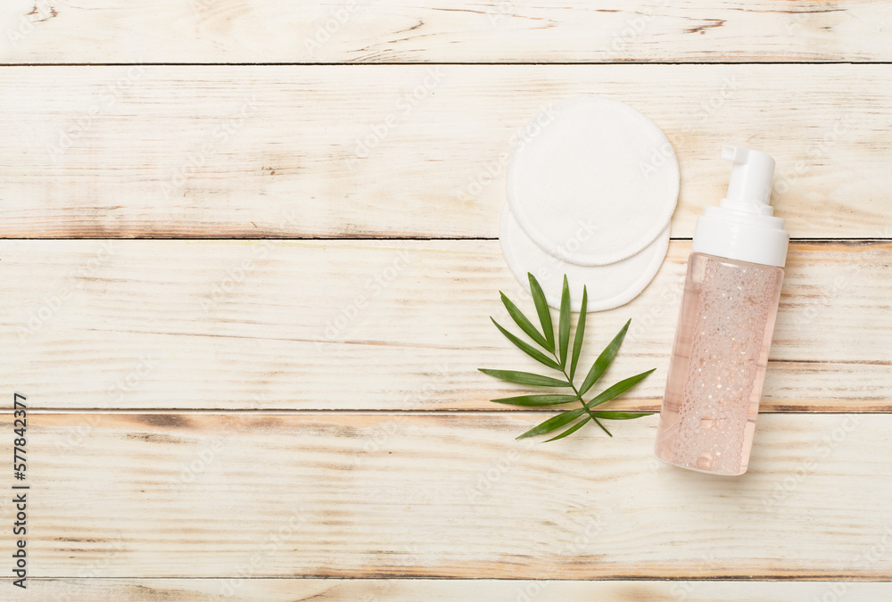 Foaming facial cleanser and with eco pads on wooden background, top view