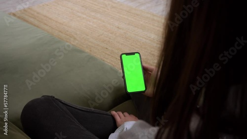 Close up of using smartphone with green screen and scrolling while sitting in room. Female holding black mobile phone with chroma key in hand, tech concept. Video 4K.