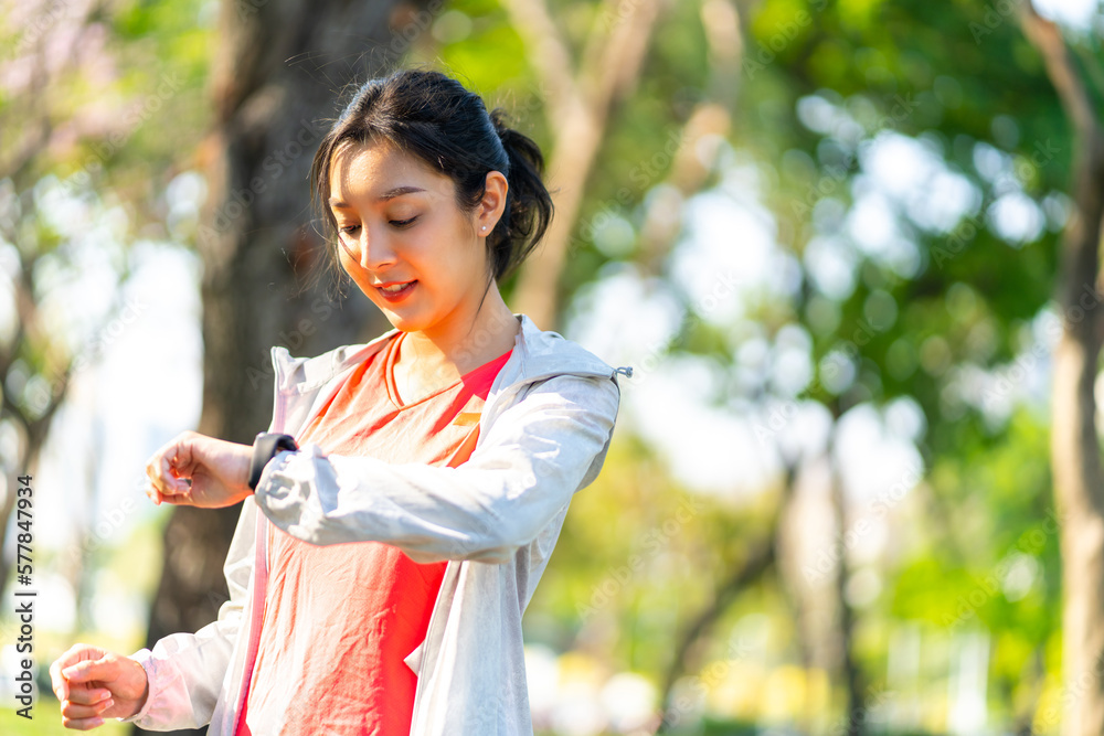 Young Asian woman in sportswear using smart watch during jogging exercise at public park. Attractive girl do sport training running workout in the city. Health care motivation technology concept. Young Asian woman in sportswear using smart watch during jogging exercise at public park. Attractive girl do sport training running workout in the city. Health care motivation technology concept.