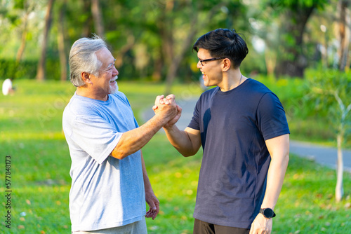 Happy Asian adult son and elderly father jogging exercise together at park. Retired man with outdoor lifestyle sport workout in the city. Family relationship and senior people health care concept.