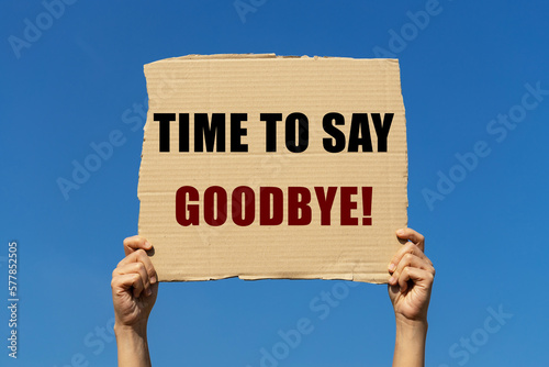 Time to say goodbye text on box paper held by 2 hands with isolated blue sky background. This message board can be used as business concept to say to others it is time to say goodbye. photo