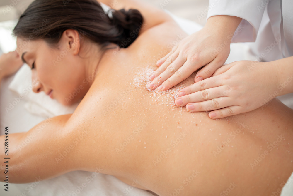 Therapist lady applying mineral sea salt on young indian woman spine Therapist lady applying mineral sea salt on young indian woman spine