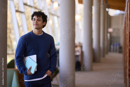 Confident portrait of a thoughtful smiling young Hispanic male student visiting a modern library