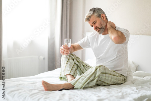Tablou pe pânză Tired man suffering from neck pain at home in bedroom