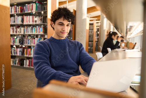 Fotografie Latin American male student using laptop, making researches on internet in moder