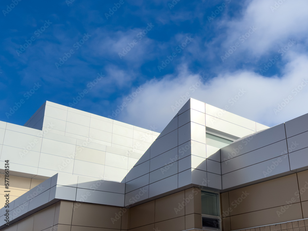 Commercial external metal composite panels on a building with blue sky and clouds in the background. The durable metal composite panels are two shades of grey in color on the modern building.