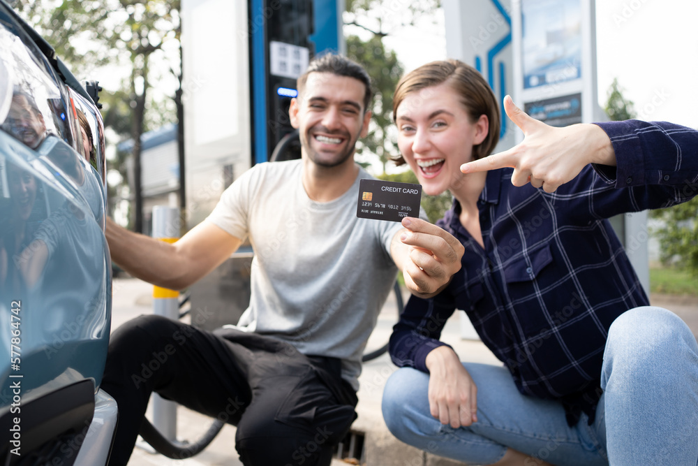 Young couple holding black credit card an electric car charging station. Young couple holding black credit card an electric car charging station.