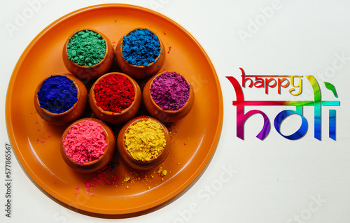 Various Holi paints in pots on a tray with a colorful inscription Happy Holi. Colorful background for the national Indian holiday Happy Holi. White background, top view.
