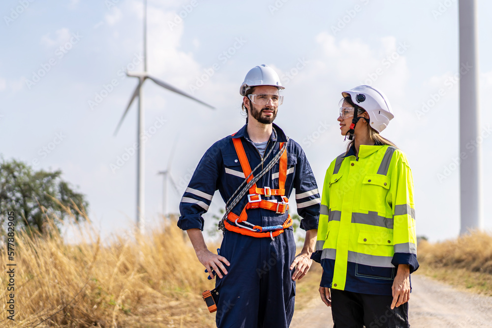 Caucasian engineer man discuss together with co-worker woman and stay in front of row of windmill or wind turbine with sky, wind turbine generate electricity, Environmentally friendly. Caucasian engineer man discuss together with co-worker woman and stay in front of row of windmill or wind turbine with sky, wind turbine generate electricity, Environmentally friendly.