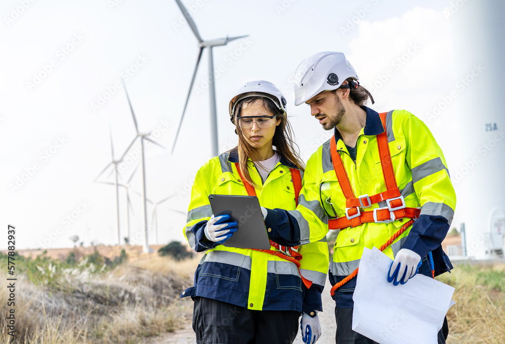 Two engineers caucasian man and woman in hardhat and goggles talk about system installation and walking to verify that a wind turbine is running correctly and effectively, Renewable energy Two engineers caucasian man and woman in hardhat and goggles talk about system installation and walking to verify that a wind turbine is running correctly and effectively, Renewable energy