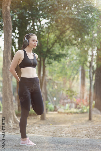 A young female athlete, dressed for running, is shown stretching her legs in preparation for a jog through the park.