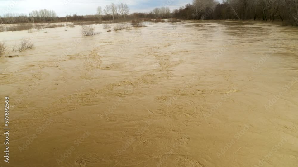 Flood A wide, muddy river with muddy, orange water after rain has overflowed and burst its banks. An environmental disaster. The problem of global warming. Weather disaster Flood A wide, muddy river with muddy, orange water after rain has overflowed and burst its banks. An environmental disaster. The problem of global warming. Weather disaster