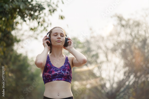 A relaxed woman is shown enjoying music while jogging through a public park. The young lady is feeling free, relaxed, and happy.