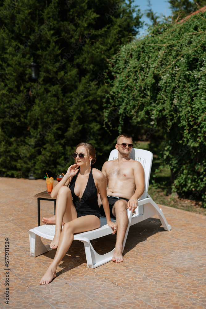 guy and a girl in bathing suits are relaxing, near the blue pool