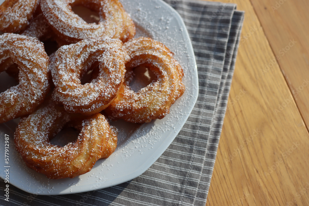 Top view of fried Zeppole with cinnamon and powdered sugar. Neapolitan homemade sweet pastry on white plate on table Top view of fried Zeppole with cinnamon and powdered sugar. Neapolitan homemade sweet pastry on white plate on table