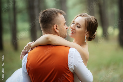 young couple bride in a white short dress and groom in a gray suit in a pine forest © omelnickiy