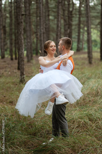 young couple bride in a white short dress and groom in a gray suit in a pine forest