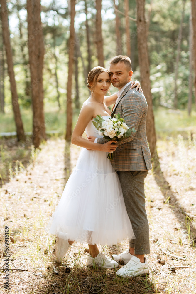 young couple bride in a white short dress and groom in a gray suit in a pine forest