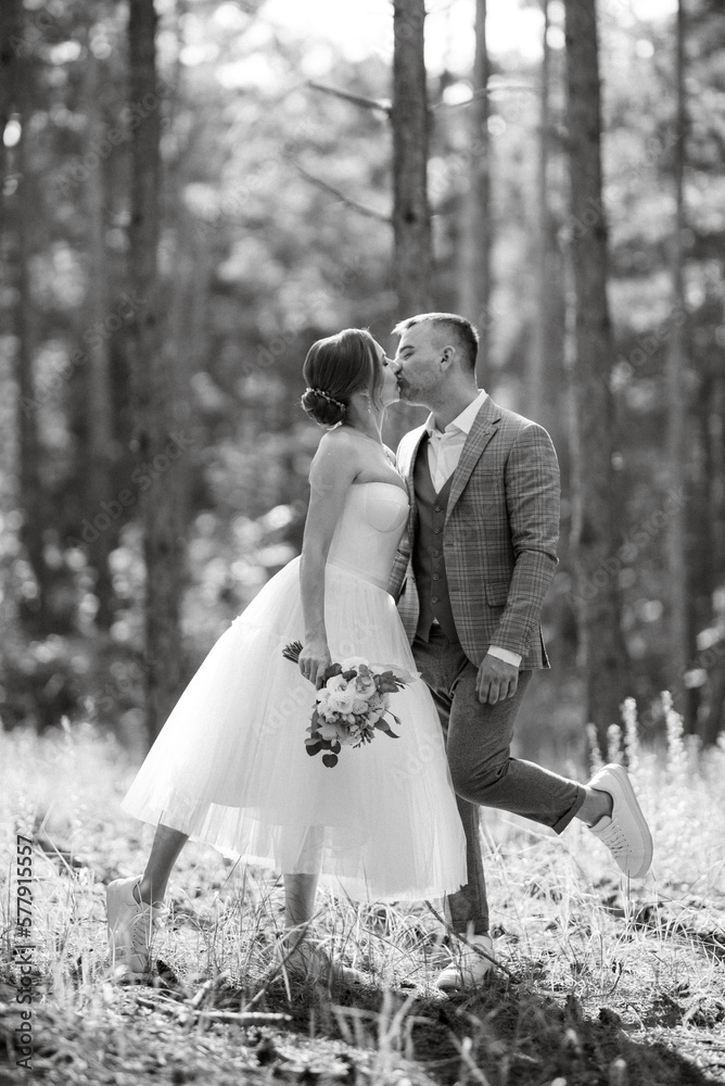 young couple bride in a white short dress and groom in a gray suit in a pine forest young couple bride in a white short dress and groom in a gray suit in a pine forest
