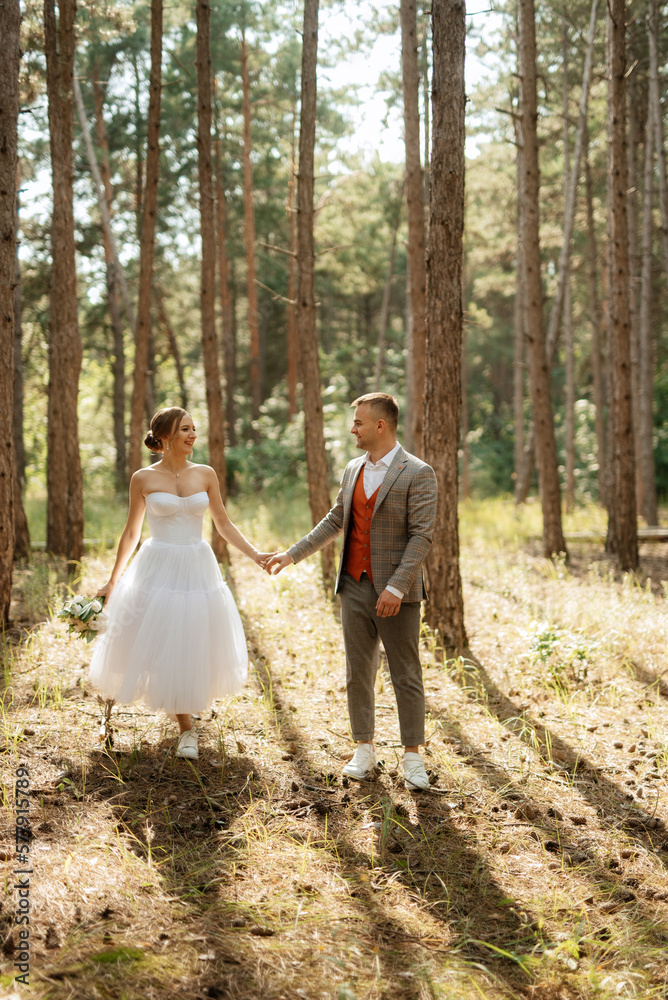 young couple bride in a white short dress and groom in a gray suit in a pine forest