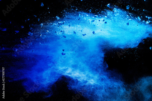Split debris of stone exploding with blue powder against black background.