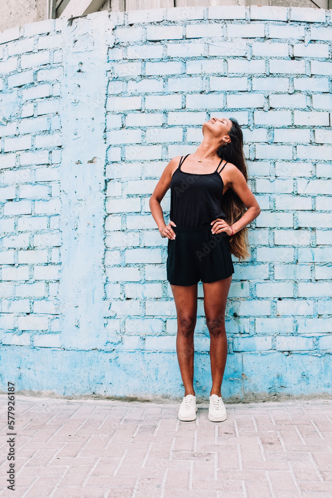 Full length of latin woman standing against a blue brick wall