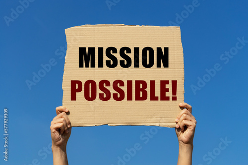 Mission possible on box paper held by 2 hands with isolated blue sky background. This message board can be used as business concept about informing people that anything is possible.