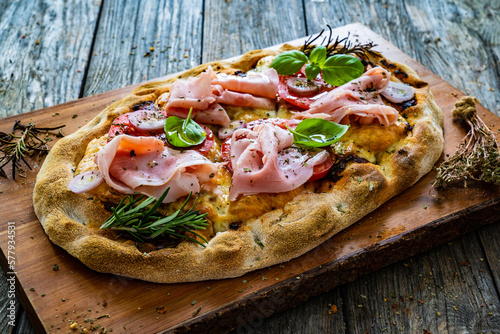 Pinsa Romana with cooked ham, mozzarella and vegetables on wooden table photo