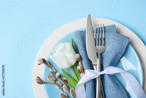 Festive table setting with willow twigs and tulip on light blue background, top view with space for text. Easter celebration #577938719