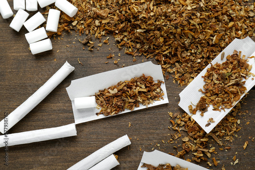 Hand rolled cigarettes, filters and tobacco on wooden table, flat lay