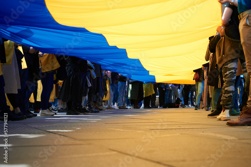 A crowd of people holding a large national Ukrainian flag at a peaceful demonstration in support of Ukraine against Russia's military aggression