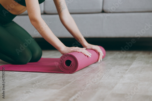 Fotografie Cropped close up side view young strong sporty athletic fitness trainer instructor woman wear green tracksuit train unroll purple yoga mat on floor at home gym indoor Workout sport motivation concept