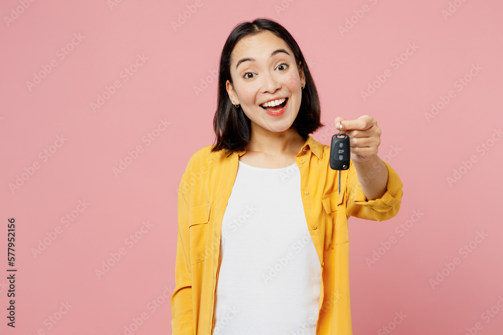 Young happy fun woman of Asian ethnicity wear yellow shirt white t-shirt hold in hand give car keys fob keyless system isolated on plain pastel light pink background studio portrait Lifestyle concept Young happy fun woman of Asian ethnicity wear yellow shirt white t-shirt hold in hand give car keys fob keyless system isolated on plain pastel light pink background studio portrait Lifestyle concept