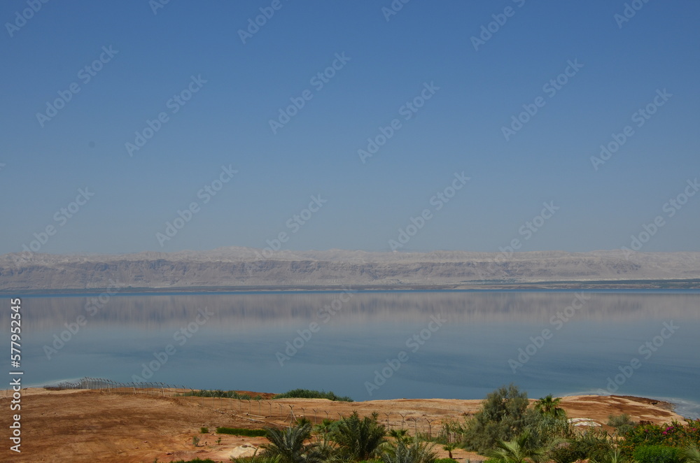 Panoramic view of the beautiful, clear blue Dead Sea shimmering and shining on a bright sunny day in Jordan and the dry land around it.