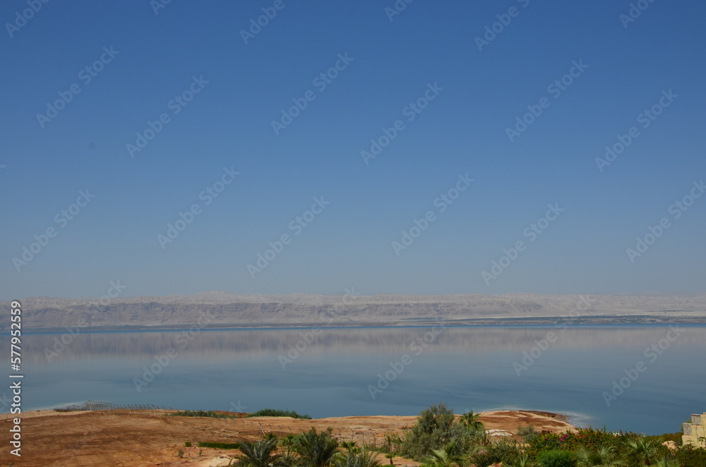 Panoramic view of the beautiful, clear blue Dead Sea shimmering and shining on a bright sunny day in Jordan and the dry land around it.