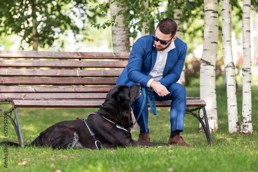 Young man in business suit wearing sunglasses speaking with his dog at walk