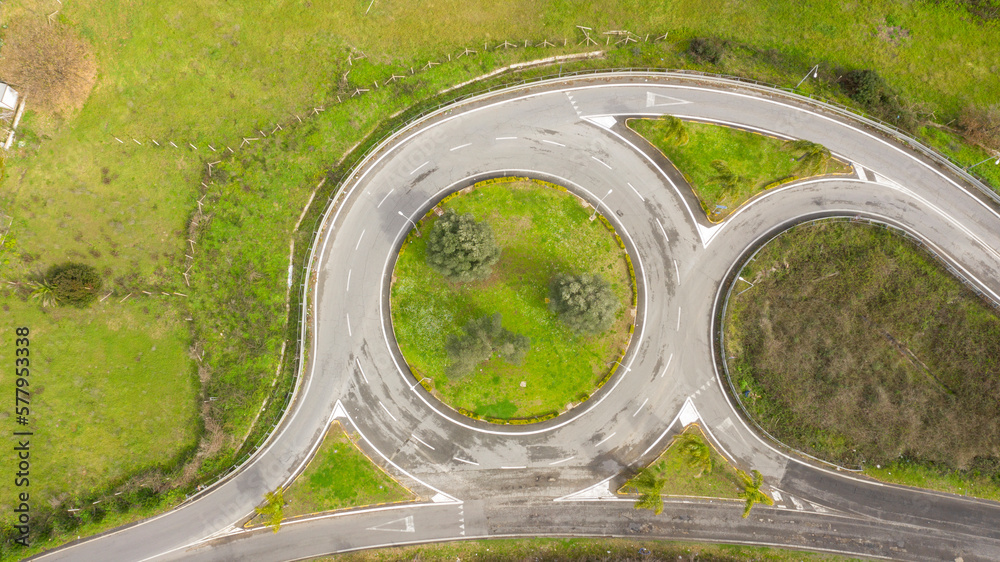 Aerial view on a roundabout road junction. Inside the rotunda a flowerbed with grass and trees. Aerial view on a roundabout road junction. Inside the rotunda a flowerbed with grass and trees.