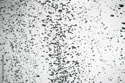 A lot of dark air bubbles of different sizes underwater on a white isolated background. Close up of light lit oxygen bubbles flow upwards. Aeration or filtration of liquid. Fizzy flow of air bubbles.