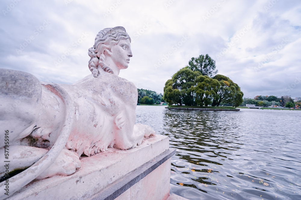 Ancient park sculpture - the Sphinx on the background of the lake. Island with trees on the lake in Moscow park. Ancient park sculpture - the Sphinx on the background of the lake. Island with trees on the lake in Moscow park.