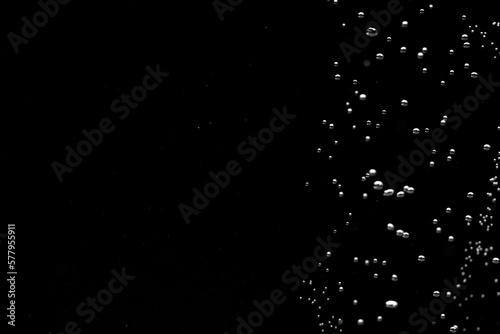 Shiny air bubbles in the right side of the frame on a black isolated background. Background with oxygen bubbles and workspace, mockup. Close up of a bubbling liquid. Fizzy flow of air bubbles.