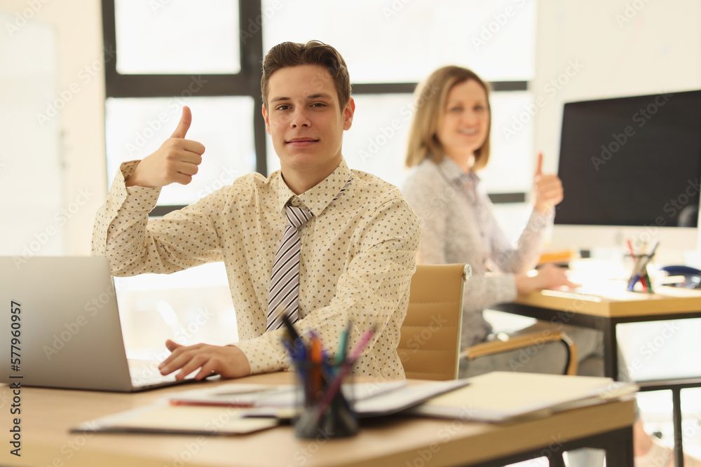 Two managers are sitting at their desks in office and showing thumbs up gesture. Two managers are sitting at their desks in office and showing thumbs up gesture.
